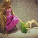 a barbie doll sitting next to a green cup