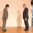 two men in suits standing in front of a white wall